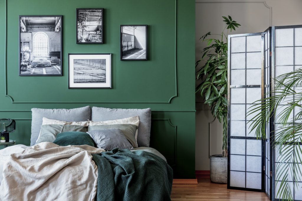 Gallery of black and white posters and photos on emerald green wall in trendy bedroom