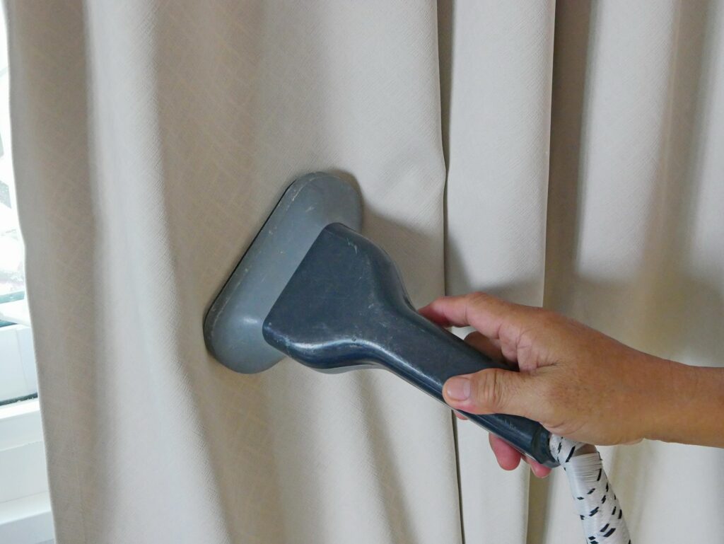 A hand of a man holding on a garment steam head while doing a steam clean for house curtains